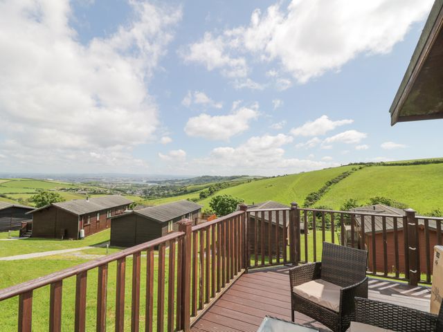 A wooden deck with chair and railing overlooking green hills and wooden lodges at Lodge 16 Whitsand Bay near Millbrook