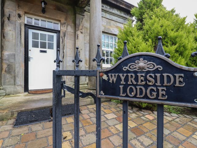 An iron gate with a sign reading Wyreside Lodge in front of a stone building with a white door and window at The Lodge House in Dolphinholme near Galgate