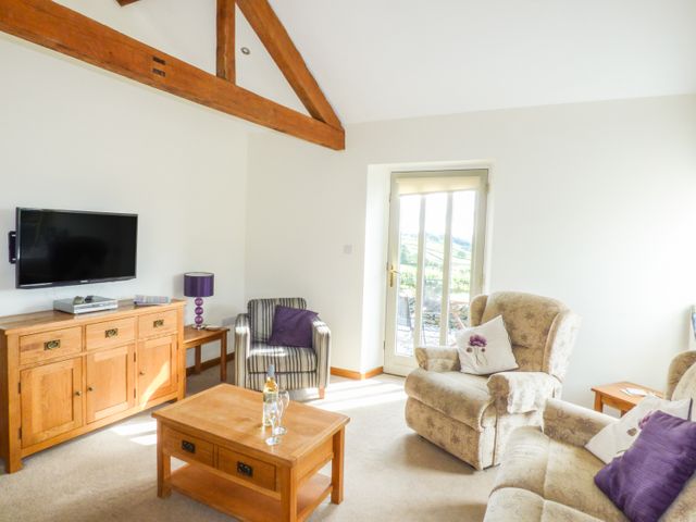 A sitting room with wooden furniture including a coffee table cupboard and two armchairs at Ghyll Bank Byre in Staveley