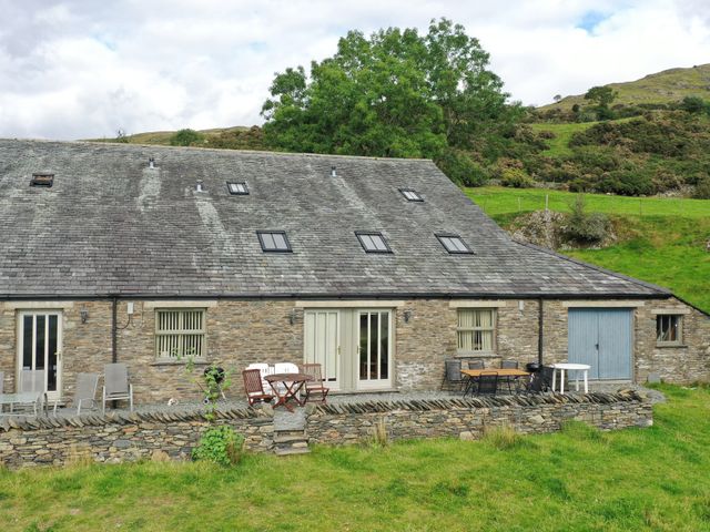 A stone house with a slate roof and multiple skylights with outdoor tables and chairs on a stone patio at Ghyll Bank Byre in Staveley