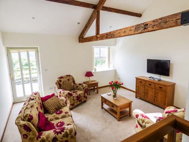 A living room with floral patterned sofa and armchairs a wooden coffee table with flowers a television on a wooden cabinet and exposed wooden beams at Ghyll Bank Barn in Staveley near Windermere