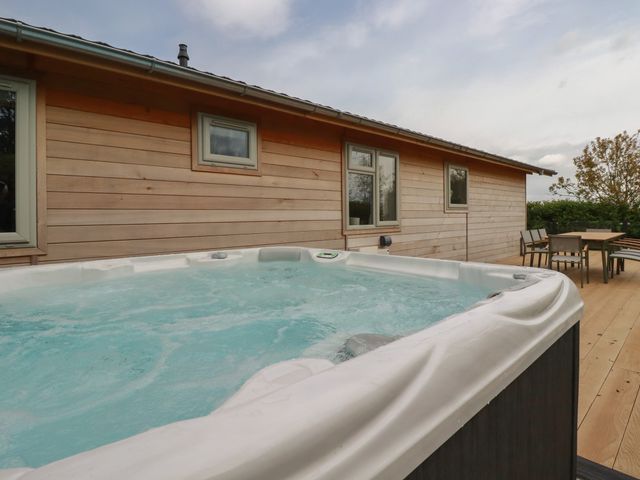 An outdoor wooden deck with a hot tub and a dining table with chairs at 6 Faraway Fields in Dobwalls