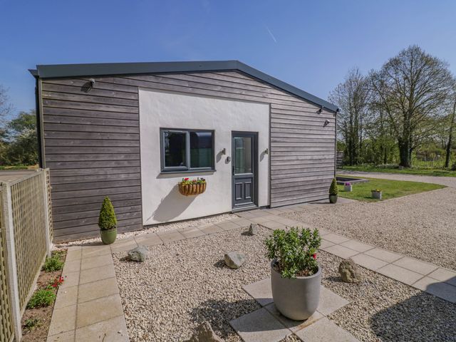 A house with wooden siding and a gray door surrounded by gravel and potted plants at Oldwyche Barns in Kineton