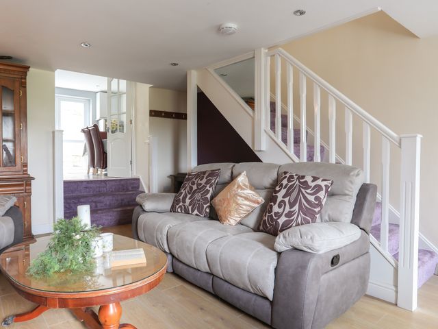 A living room with a sofa, a wooden coffee table, and stairs with a white banister at 43 Hyfrydle Road Penygroes