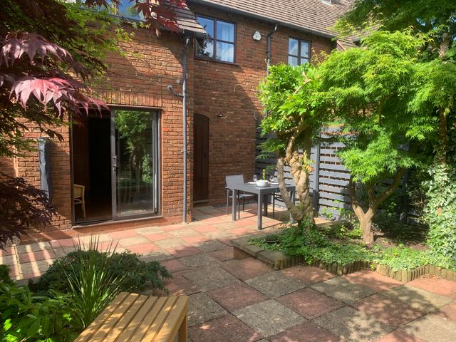 A patio with a wooden bench a small dining table with chairs and potted plants outside a brick house at Old Town Cottage Stratford-Upon-Avon