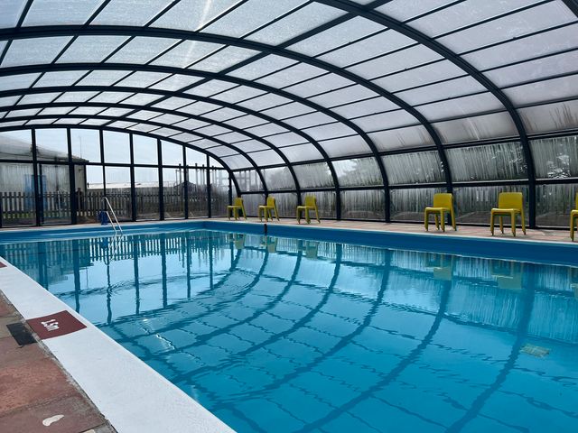 An indoor swimming pool with a glass curved roof and yellow chairs along the sides at Chalet 2 at Landscove Holiday Park in Brixham