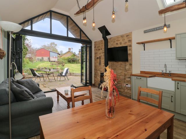 An open plan kitchen and living area with wooden dining table and chairs a gray sofa wood burning stove and glass doors opening to a patio at The Cart Shed in Barwick near Yeovil Somerset
