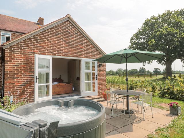 An outdoor patio with a hot tub table chairs and umbrella next to a brick house with open doors showing a wooden bed inside at Orchard View in Redmary DAbitot near Hartpury