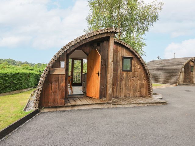A wooden arched cabin with an open door and a wooden porch area at Kingfisher in Llangammarch Wells near Beulah