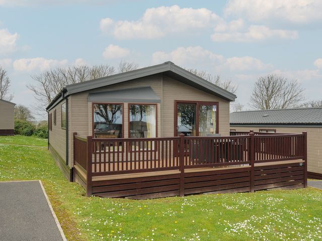 A single-story wooden cabin with a fenced front porch on a grassy area at Lodge 66 at Riviera Bay Coastal Retreat in Brixham