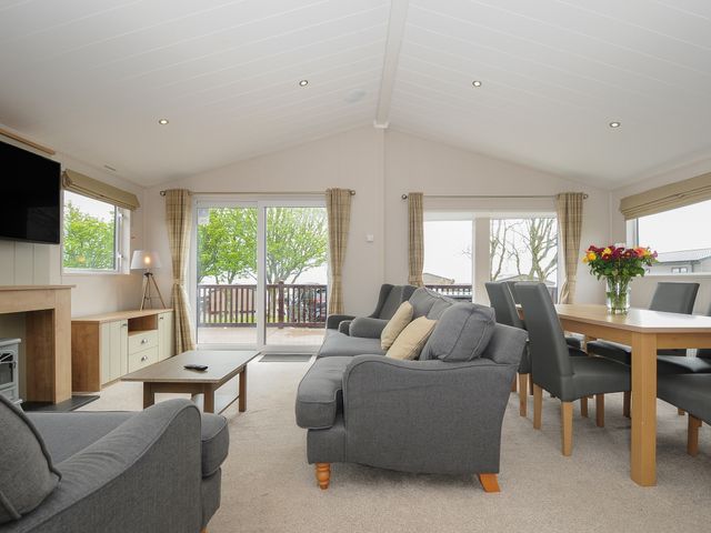 A living room with grey sofas, a wooden coffee table and a dining table with chairs and flowers on top at Lodge 64 at Riviera Bay Coastal Retreat in Brixham