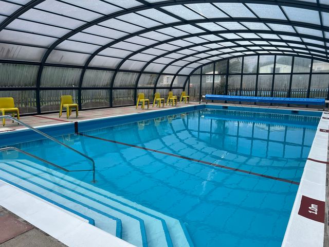 An indoor swimming pool with stairs and yellow chairs along the side at Lodge 9 at Landscove Holiday Park in Brixham