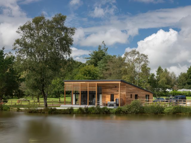 A wooden house near a lake with trees and cars at Silver Birch in Dolton