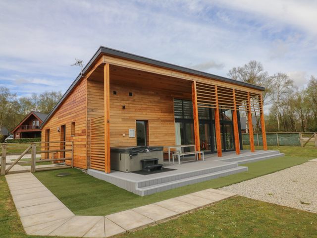 A wooden house with a covered patio with a hot tub and outdoor table and bench at Cherry in Dolton