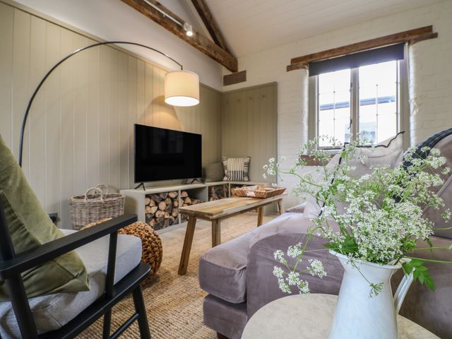 A living room with a sofa, armchair, TV, wooden coffee table, basket, and flowers in a vase at Beech Cottage - Fold Yards in Alderwasley near Crich