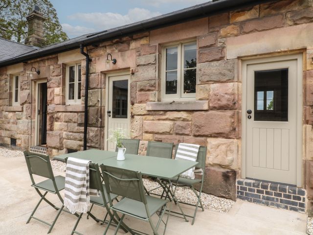 An outdoor patio with a green table and chairs against a stone building wall at Hazel Cottage - Fold Yards in Alderwasley near Crich