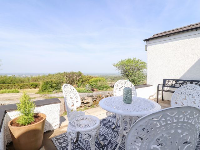 An outdoor patio with white metal table and chairs a planter with a small tree and a bench at Tan Y Merddyn in Ceunant near Llanrug