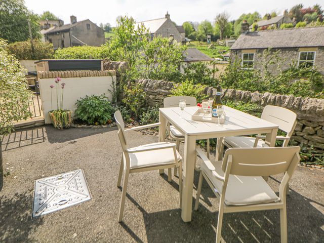 An outdoor patio with a square table and four chairs with glasses and a bottle on the table surrounded by stone walls and houses at The Cottage Bradwell in Bradwell