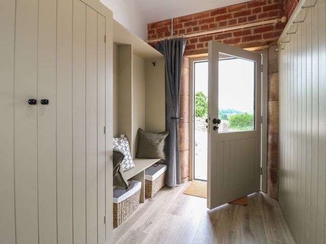 A hallway with built-in storage cabinets benches with cushions and baskets an open door showing outside at Alder Cottage - Fold Yards in Crich