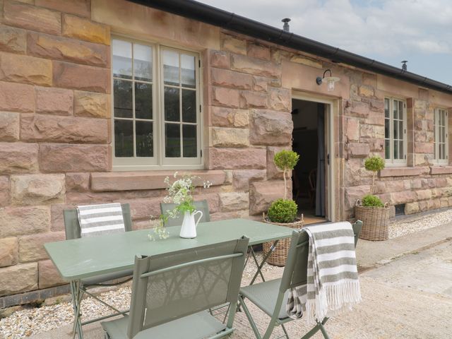 An outdoor seating area with green chairs and table in front of a stone building with windows and potted plants at Oak Cottage - Fold Yards in Crich