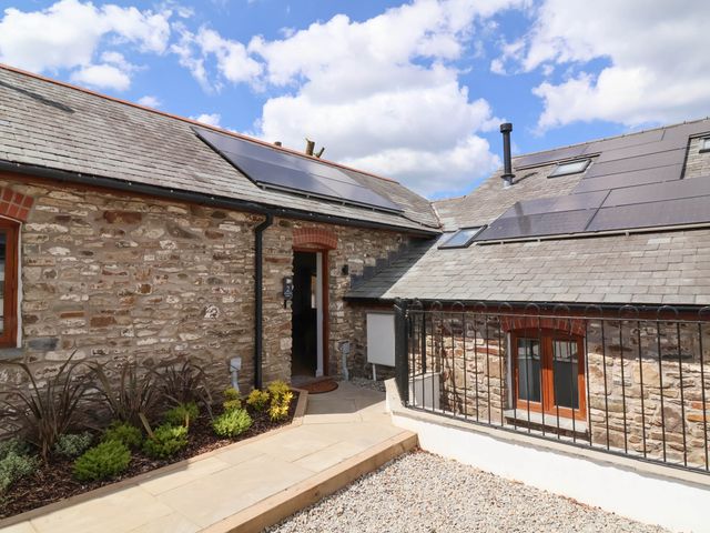An exterior view of a stone building with solar panels on the roof and a small garden bed at Woodland Roost in Parkham near Bideford