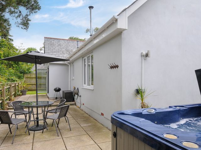 An outdoor patio with a round table and chairs under an umbrella a barbecue and a hot tub at Seagrass in Bideford