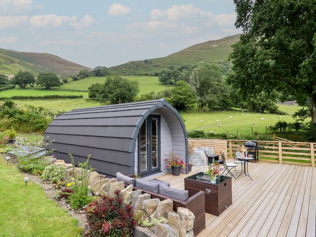 A cabin with a deck and furniture near a green landscape at Caban Tirion in Dinas Mawddwy near Dolgellau