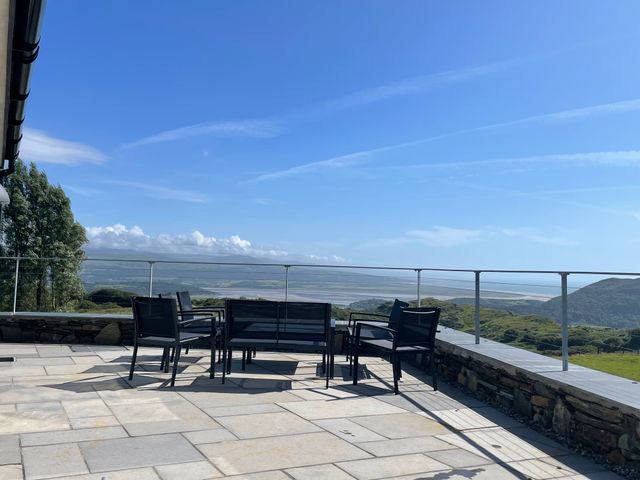 An outdoor patio with black chairs and a table overlooking hills and a coastline at Beudy Mawr in Cwmystradllyn near Tremadog