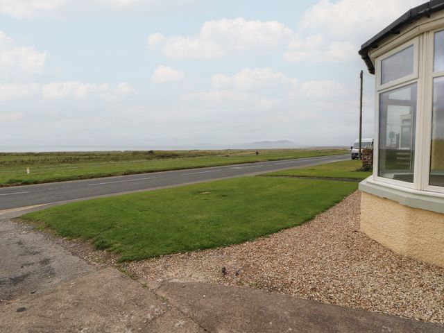 A view of a grassy area and a road with a house corner in the foreground at Burnbank in Allonby near Maryport