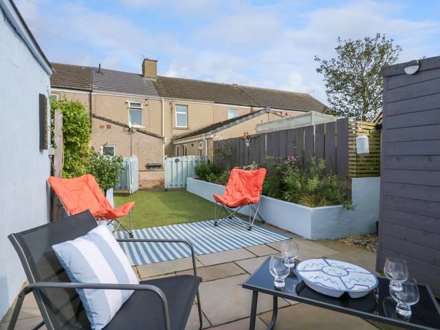 A backyard with patio chairs and table with glasses and a bowl at Willow Cottage in Haverigg