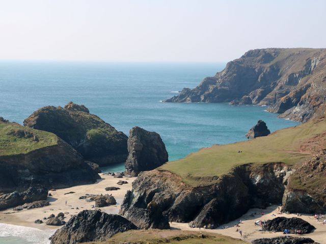 A beach with rock formations and people at the shore near Lizard
