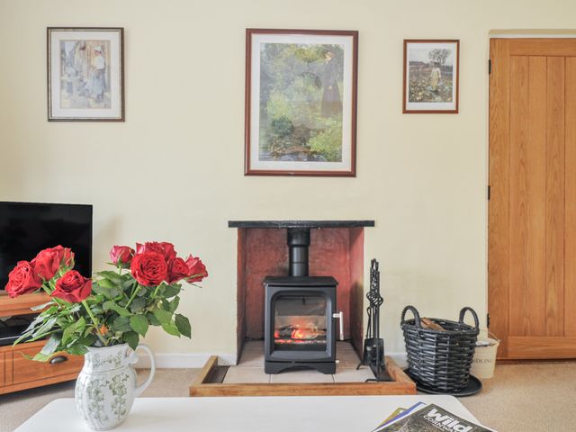 A living room with a fireplace and a vase of roses at Jordan Cottage in Fowey