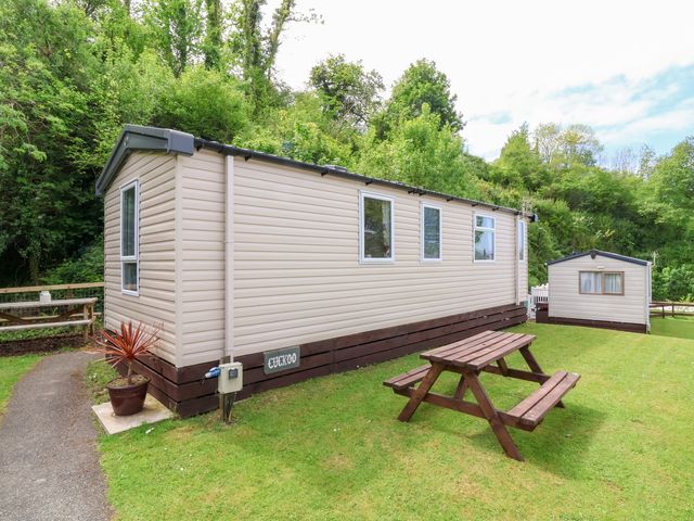 A mobile home with a picnic table on grass and trees in the background at 25 Manleigh Park in Combe Martin