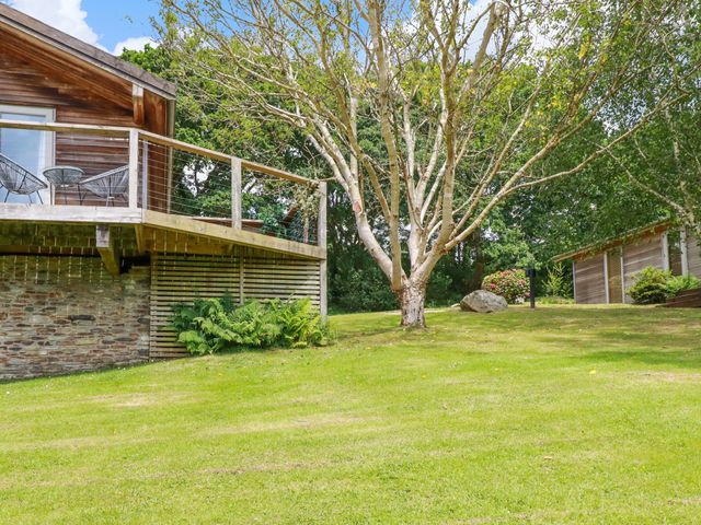 A grassy garden with trees and wooden houses with a deck and two chairs at 3 Lake View in Lanreath