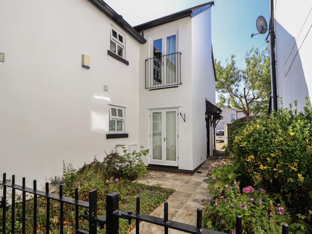 The exterior of a white building with black trim near a paved pathway and garden with plants and flowers at The Stocks in Newtown-le-Willows