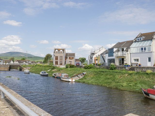 A river with several small boats moored beside it and houses along the opposite bank at Lazey Cottage in Haverigg