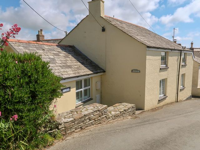 A yellow house with a stone wall and a sign at Hilldene in Treknow