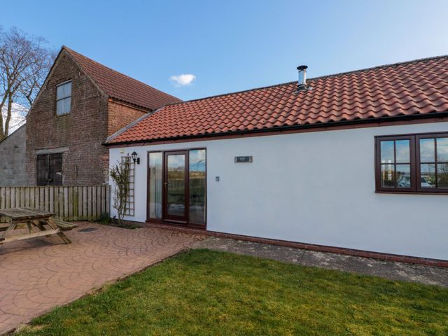 A cottage with tiled roof white walls wooden door and window with grassy lawn and wooden picnic table nearby at Partridge Cottage neaer Filey