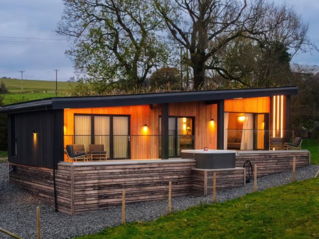 A modern cabin with wooden exterior and glass doors with outdoor seating and a hot tub at The Lookout in Longridge