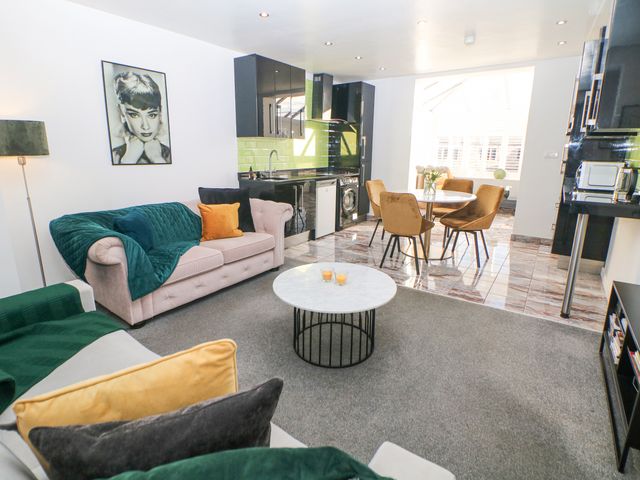 A living room with sofas cushions a coffee table and a kitchen with black cabinets and a dining table with chairs at Number 4 Westmoreland in Two Dales