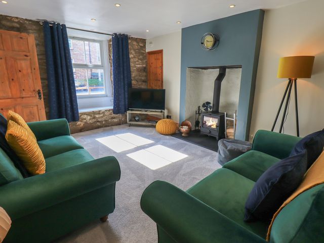 A living room with green sofas a wood burning stove and a TV at Fettlers Cottage 51 High Street Kirkby Stephen
