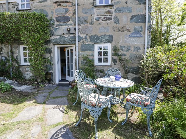 A garden area with a round metal table and four chairs outside a stone house at Pen Y Bryn Bach in Harlech