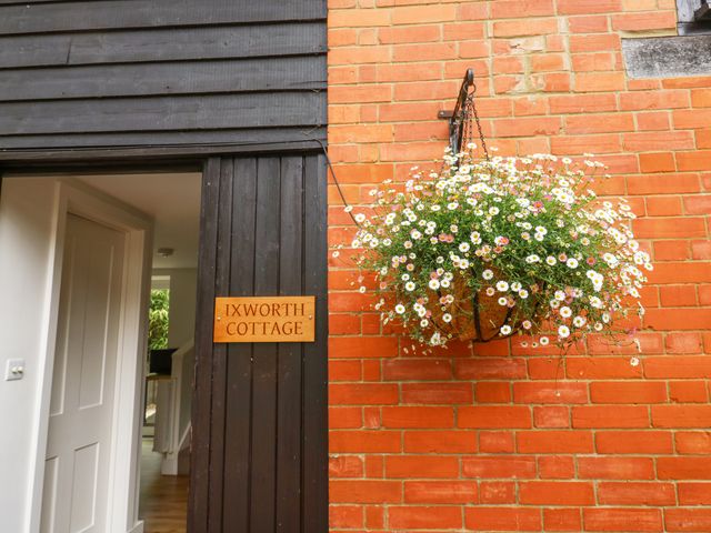 An open door with a wooden sign reading Ixworth Cottage and a hanging basket of flowers on a brick wall at Ixworth Cottage in Little Woodford near Ottery St Mary