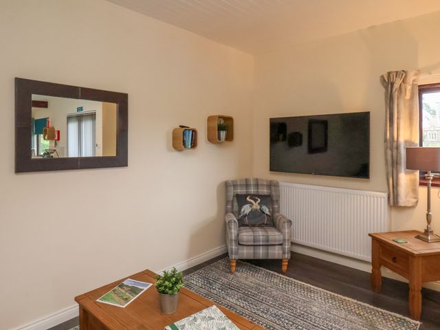 A sitting area with a plaid armchair cushion a wall-mounted tv two wooden tables a lamp rectangular mirror and small shelves on the wall at Ramson in Saltburn-By-The-Sea