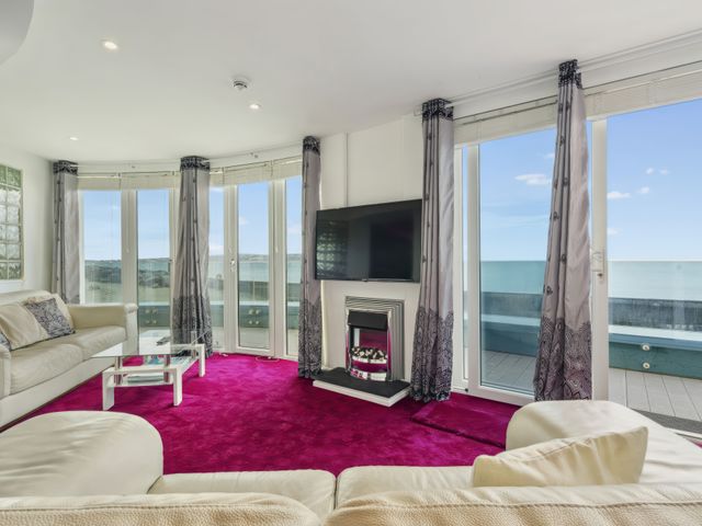 A living room with white sofas a glass coffee table a mounted television and large windows overlooking the sea at Blue Horizon in Milford On Sea