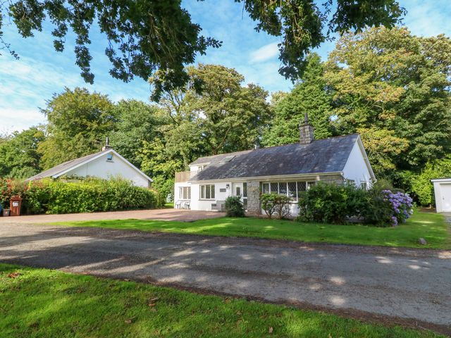 A detached house with white walls and a slate roof surrounded by trees and grass at Ty'r Glyn in Llanbedrog