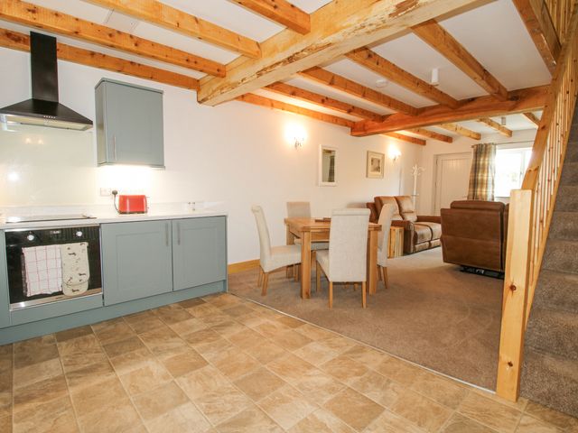 A kitchen with gray cabinets and a dining table in an open plan living area with exposed wooden beams at Chester in Knolton near Ellesmere