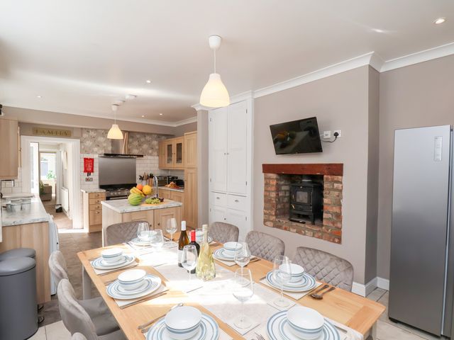 A kitchen dining area with a wooden table set for six a fireplace with a stove and a mounted television at Tennyson Grange in Bridlington