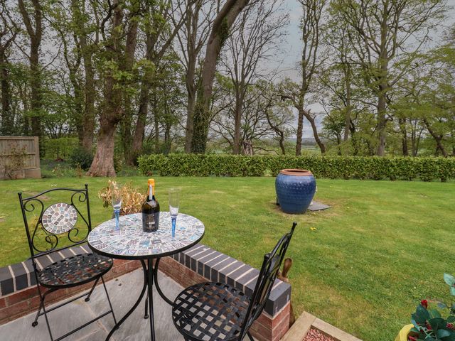 A garden patio with a mosaic table, two chairs, a bottle, and two glasses with trees and a blue pot in the background at The Nest in Wetheral