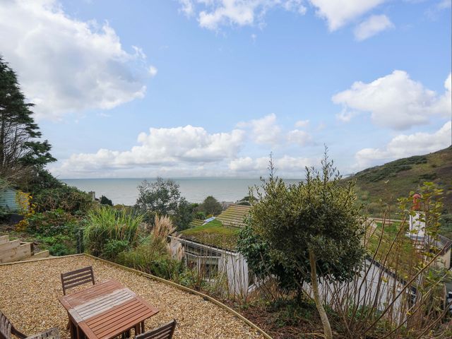 An outdoor seating area with a wooden table and chairs overlooking plants rooftops and the sea at Waves Edge in Looe